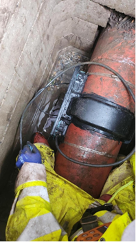 Image of a pipeline running parallel with a brick wall with a tight gap between them where Atmos' hardware instrumentation is being successfully installed by an engineer